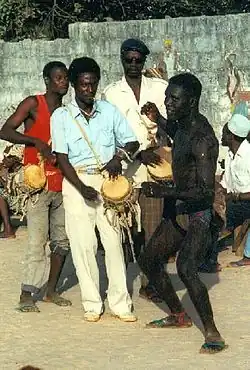 A shirtless man in a wrestling pose next to three drummers.