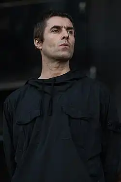 A middle-aged man with dark hair and blue eyes looks to the side.