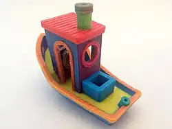 A multi-material 3DBenchy created on a Prusa i3 using a color-mixing hot end; each part of the boat has been created in a different colour.