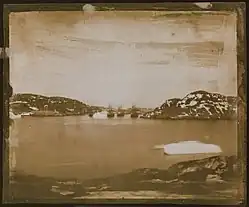 a sepia toned photographic view of four ships in the distance sailing through a channel.
