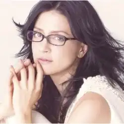 A woman wearing black glasses on a pale pink background.