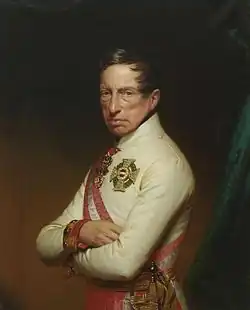 Painting shows a frowning man in a white military uniform with his arms folded.