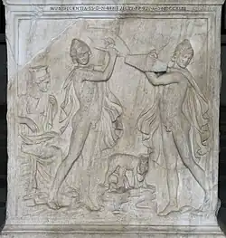 Two men holding shields stand in front of a baby drinking the milk of a goat