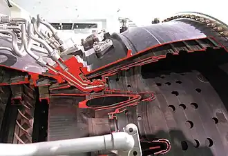 JT9D straight-through annular combustor, airflow from left to right. The atomizing fuel nozzle is a dual orifice or duplex type. The primary, or pilot flow, comes from a small hole (orifice) in the centre at low engine speeds through the fuel tube at the left. The secondary, or main flow, comes from a larger opening around it at higher speeds through the tube on the right. Airflow from the small compressor exit guide vane at the left enters an area-increasing diffuser which divides it into three parts. The centre flow enters the combustor and mixes with fuel. The outer and inner parts enter the combustor progressively through the holes shown completing the combustion and then diluting to give a final exit temperature suitable for the turbine.