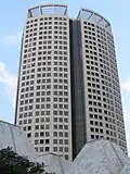 Ground-level view of a 40-storey skyscraper with a rounded facade and an open, lattice-work structure on the roof