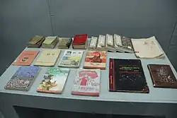 A table in a museum with various weathered Chinese textbooks. Many of their covers feature communist symbols