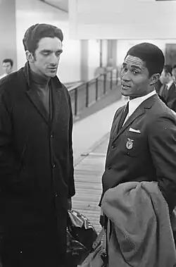 A man in a coat, talking with a man in a suit