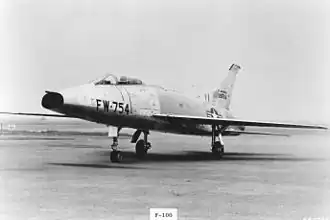 A jet aircraft with nose air intake sits on the tarmac, wearing U.S. Air Force insignia and "FW-754" coding on the nose