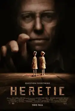 An old man wearing thick glasses reaches out towards two miniature dolls.