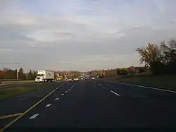 Eastbound IL 120 west of Hunt Club Road. Road is divided highway with a grassy median and open areas on both sides with scattered trees.