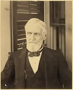 bearded man looking forward with shuttered window in background