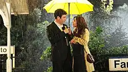 Ted and the Mother under a yellow umbrella in the rain.