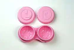 An open lens care. The lens caps are engraved with the letters L and R to indicate left and right. The case body is shaped as a pair of glasses and contains two holes for the lenses.