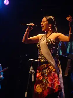 A woman in a flower dress singing to a microphone with her eyes closed.