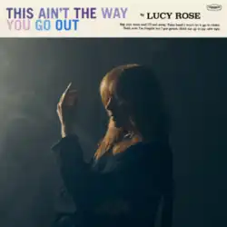 Rose sitting on a chair in a dark and smoky room with her left arm raised in front of her face