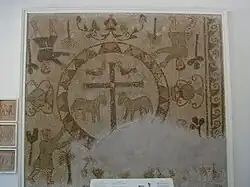 Mosaic on a wall with four figures in the corners and a large cross in the middle