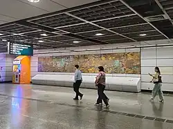 A brass mural on a wall of the walkway, with people walking past it