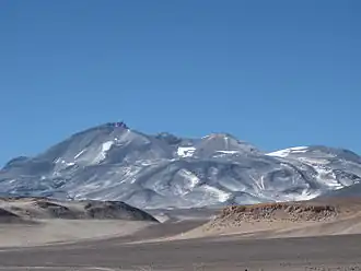 Photo: A broad, irregular mountain in an unvegetated landscape with sparse snowpatches