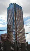 Oro, a high-rise clad in stone and blue glass with curved corners, viewed from street level