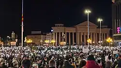 A crowd of people hold their phones up towards the sky with the flashes on.