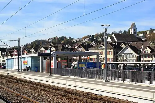 Low platform with boxy structure and houses on a hillside beyond