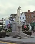 Statue on a plinth of a woman in classical dress carrying a jug on her shoulder and holding a child's hand. Steps up to the base of the plinth lead to a drinking fountain.