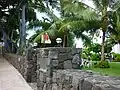 Stone wall and gate of Huliheʻ Palace with musicians in the yard. (10/2012)