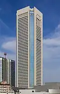 Mid-level view of a white, window-dotted, rectangular high-rise; the corners are cut and made of glass