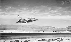 Rear quarter view of a jet fighter taking off with mountainous terrain visible in the distance