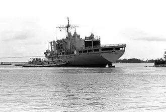 Black and white image depicting a ship being tugged back out to sea.