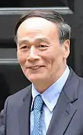 a smiling nearly bald man, wearing a suit and a blue tie